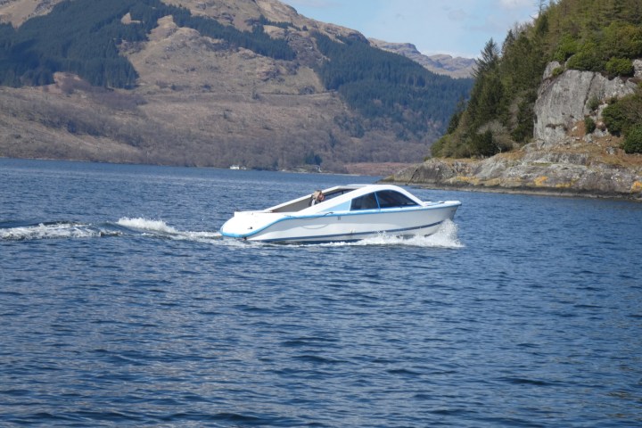 A white speedboat traveling on a lake with mountainous background.