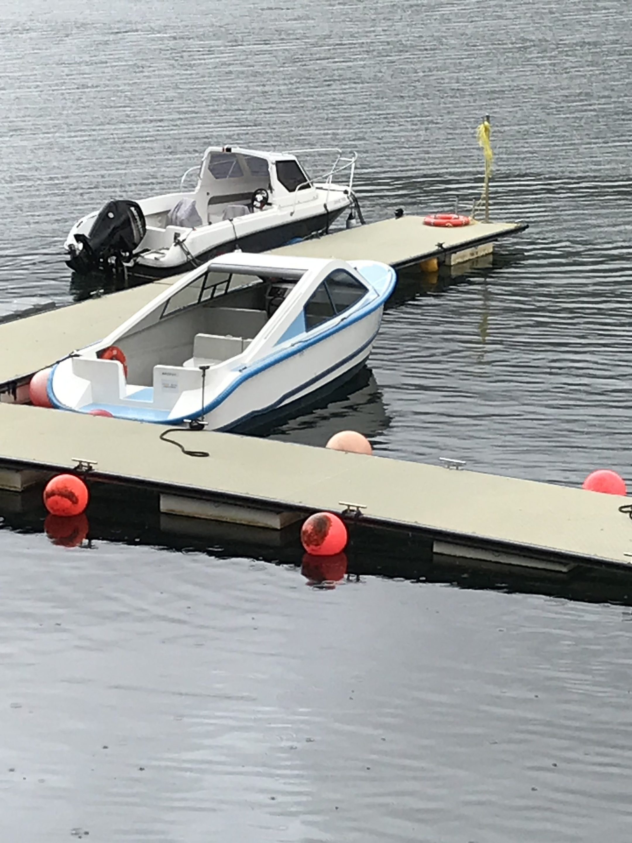 Small seaplane docked on calm water with red buoys.