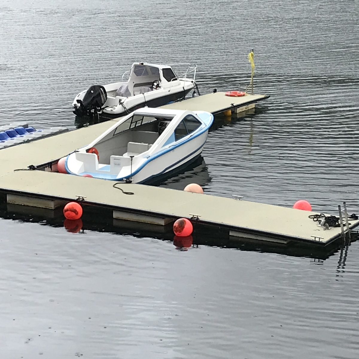 Small seaplane docked on calm water with red buoys.