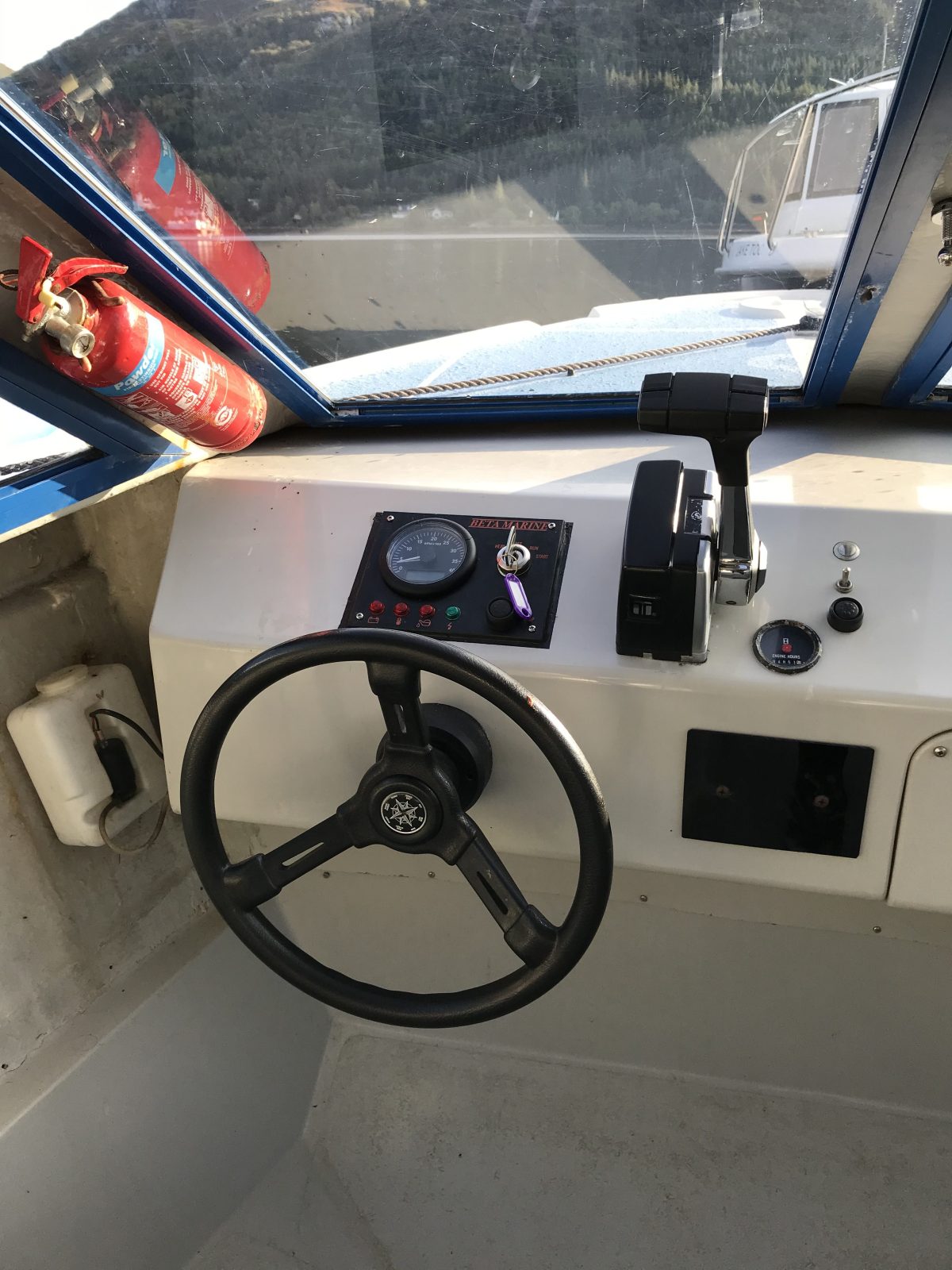 Boat cockpit with steering wheel, throttles, gauges, and a fire extinguisher.