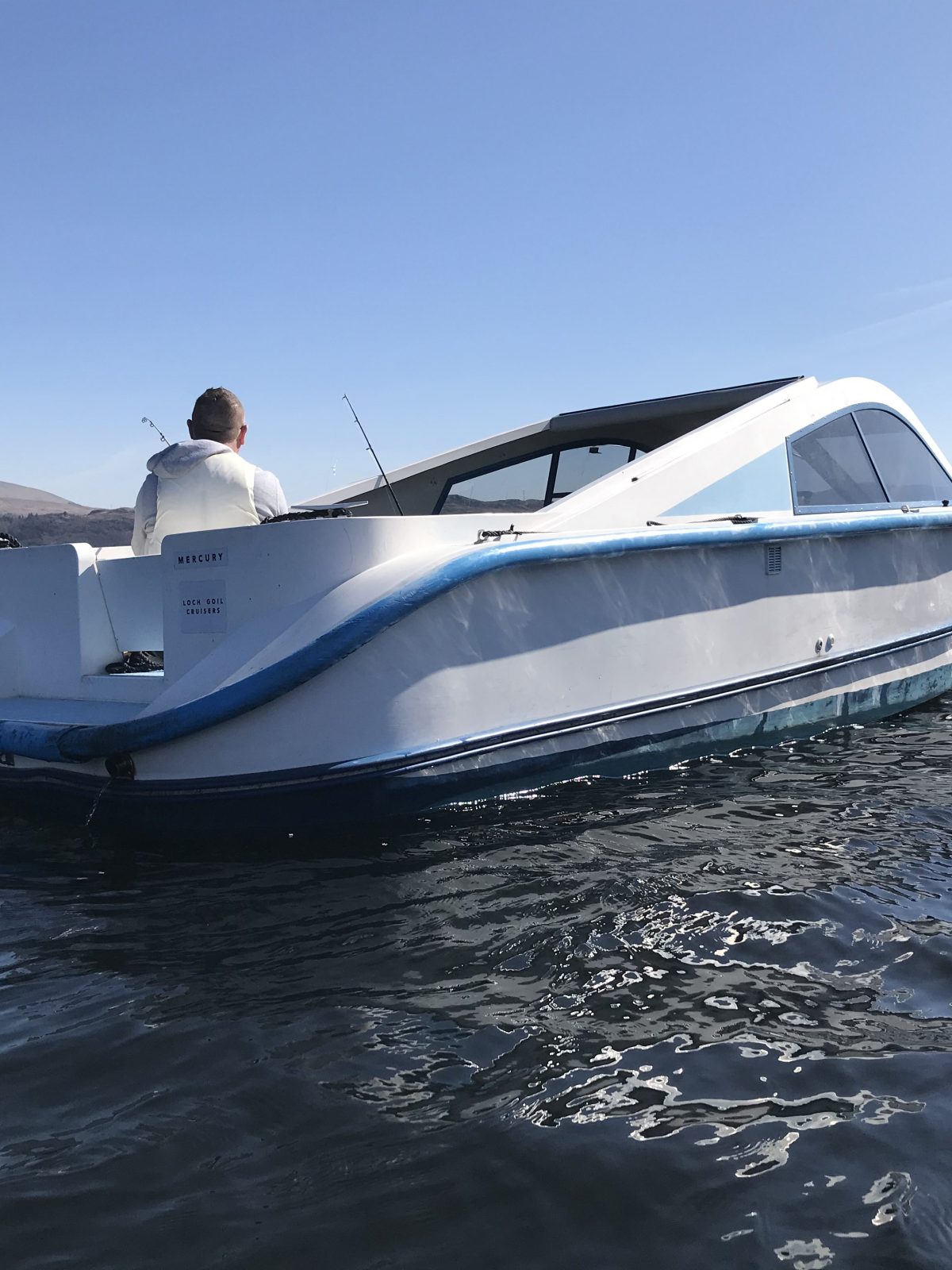 White and blue boat on calm water with hills in the background.