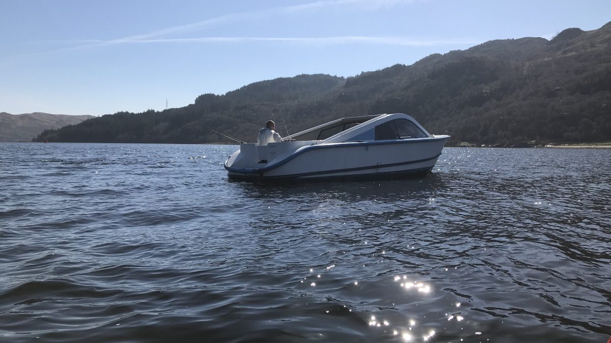 Upside-down image of a boat on a calm lake with hills in background.