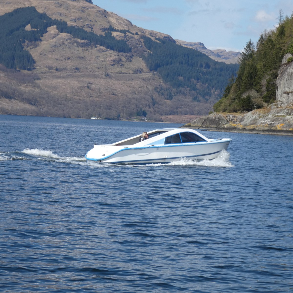 White speedboat on a lake with hills in the background.