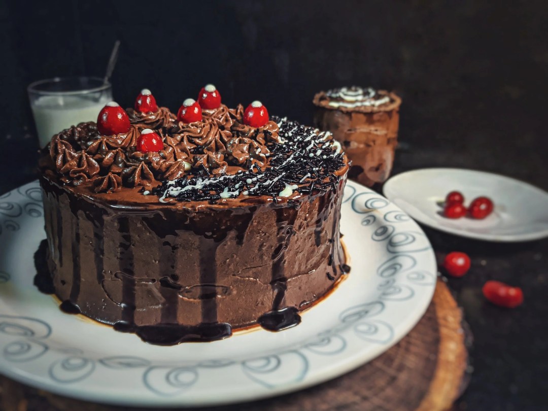 Chocolate cake with cherries on top on a white plate.